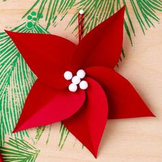 a red origami star hanging from a christmas tree with pine branches in the background