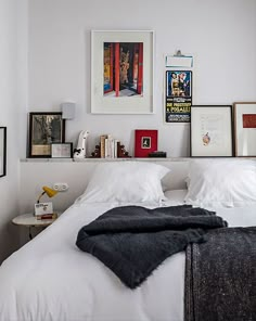 a white bed topped with pillows and blankets next to a wall filled with framed pictures