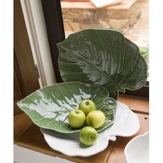 some green apples are in a bowl on a window sill next to a large leaf