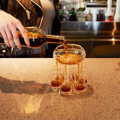 a woman pouring liquor into glasses on top of a counter