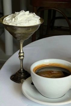 a cup of coffee on a saucer with whipped cream in the middle and a spoon next to it