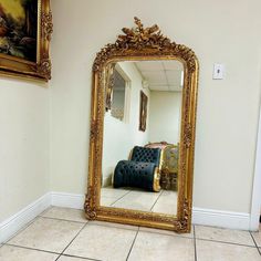 a large gold framed mirror sitting on top of a tiled floor next to a couch