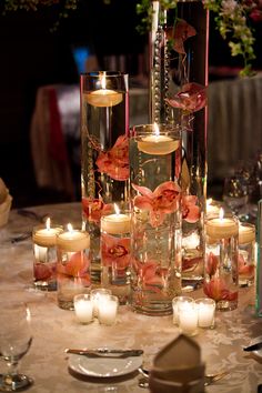 a table topped with lots of tall vases filled with flowers and lite candles