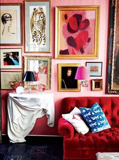 a red couch sitting in front of a pink wall covered in pictures and framed art