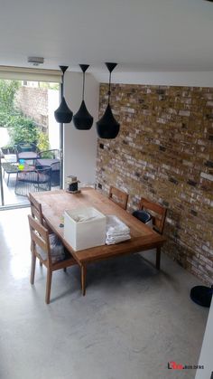 a dining room table and chairs in front of a brick wall with black hanging lights