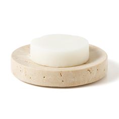 a white soap bar sitting on top of a wooden plate with a circular base and small round piece of wax next to it