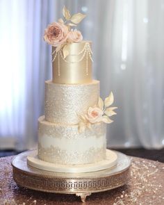 a three tiered wedding cake with pink flowers on the top and gold trimmings