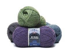 three balls of yarn sitting next to each other on a white surface, one ball is green and the other is purple