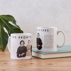 two coffee mugs sitting next to each other on top of a wooden table near a plant