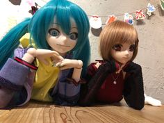 two dolls sitting next to each other on top of a wooden table in front of a wall