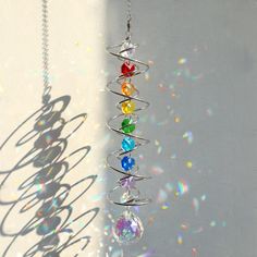 a wind chime hanging from a chain on a white wall with the sun shining through it