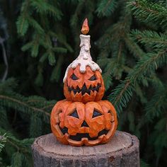 two carved pumpkins sitting on top of a stump in front of some pine trees