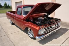 an old red pickup truck with its hood open in front of a building and grass