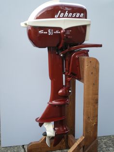 a red and white boat sitting on top of a wooden stand next to a wall