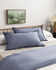 a bed with blue sheets and pillows in a bedroom next to a painting on the wall