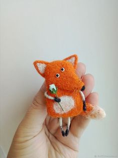 a hand holding a tiny orange fox with a flower in it's mouth