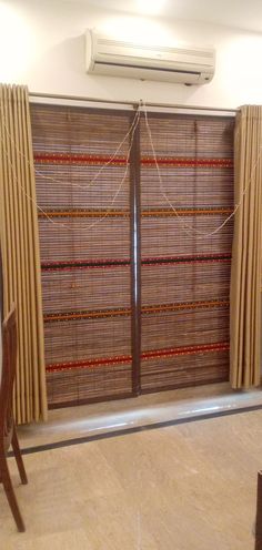 a living room with two wooden chairs and a window covered in bamboo blinds on the sliding glass doors