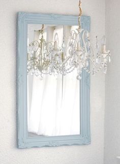 a chandelier hanging from the side of a blue frame in front of a mirror