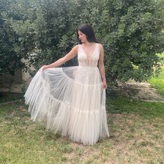 a woman in a white dress is holding her long skirt while standing outside near some trees