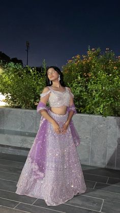 a woman in a purple and white lehenga posing for the camera at night