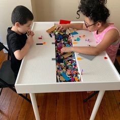 two children are playing with legos on a table in front of a white wall