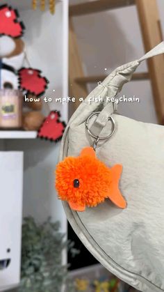 an orange pom - pom fish keychain hanging from a white bag