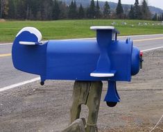 a blue mailbox sitting on the side of a road next to a tree filled field