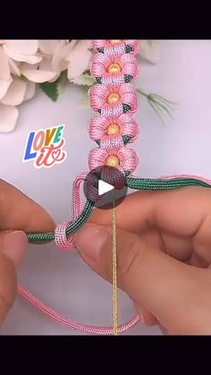 two hands are working on a beaded bracelet with pink and green beads, while another hand is holding the string