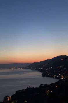 the sun is setting over some water and hills in the distance, with buildings on either side