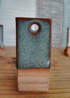 a small blue and brown vase sitting on top of a wooden table next to a window