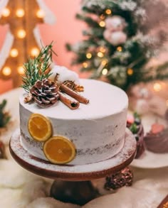 a white cake with orange slices and pine cones on top, surrounded by christmas decorations