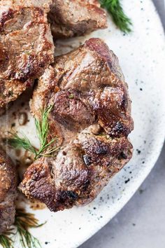 some meat on a white plate with sprigs of rosemary