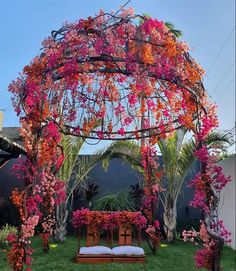 a gazebo covered in pink flowers and greenery next to a bench with pillows on it