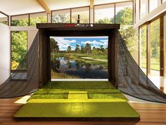 an indoor golf course with green mats and netting on the ground, in front of large windows