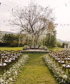 an outdoor ceremony set up with chairs and flowers on the grass, surrounded by string lights