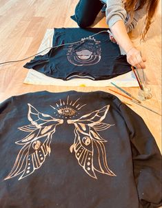 a woman sitting on the floor working on some t - shirts with scissors and thread