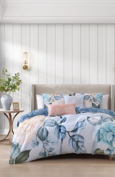 a bed with blue and pink flowers on it in a room next to a table