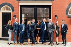 a group of people standing in front of a brick building with black doors and windows