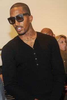 a man with tattoos and sunglasses standing in front of a group of people wearing black sweaters