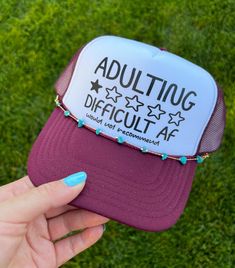 Turn heads with the Otto® 'Adulting Difficult' Foam Snapback Cap w/Chain. This unique hat features a high-quality foam front panel and breathable mesh back for ultimate comfort and style. The playful 'Adulting Difficult' graphic, combined with a trendy chain detail, adds a bold and cheeky twist to your casual look. Perfect for parties, social events, or adding a fun statement to your everyday outfit. The adjustable snapback closure ensures a perfect fit for all-day wear. Elevate your accessory game with this eye-catching and humorous trucker hat. Shop now to add this standout piece to your collection! Specs: * Fabric: 55% Foam, 45% Nylon * Closure: Plastic Snapback * Fit: One Size Fits Most * Panels: 5 * Crown: Mid; Structured * Visor: Curved The Mid Profile 5 Panel Foam Trucker Hat is con Fun Hats, Unique Hats, Custom Vinyl, Cool Hats, Snapback Cap, Trucker Cap, Everyday Outfits, Caps Hats, Casual Looks