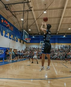 a person jumping up in the air to dunk a basketball on a court with an audience watching