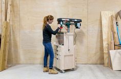 a woman using a driller on a cabinet in a room with plywood boards