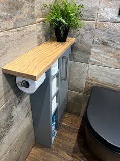 a bathroom with a toilet and a plant on the shelf next to the trash can