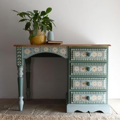 a green painted desk with drawers and a potted plant on top