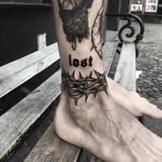 a tattoo on the foot of a person with barbed wire around their ankles that reads, lost