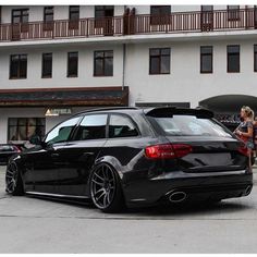 a black car parked in front of a building with two people standing around the cars