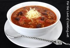 a white bowl filled with chili and cheese on top of a saucer next to a spoon