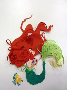 two paper cutouts of mermaids and an octopus on a white surface with fish around them