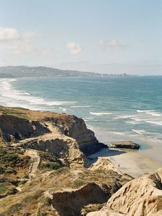 people are walking along the beach near the water's edge, with cliffs in the foreground