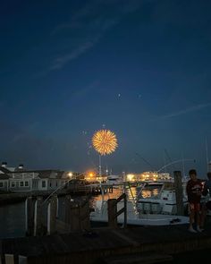 fireworks are lit up in the night sky over boats docked at a harbor with houses